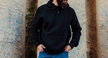 Canvas Print - City portrait of handsome hipster guy with beard wearing black blank hoodie or sweatshirt with space for your logo or design. Mockup for print