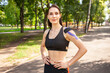 © YouraPechkin - Portrait of attractive muscular brunette woman wearing black sports outfit, looking at camera. Young smiling female athlete posing with hands on waist, colorful kinesiotaping on body.