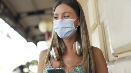 Wall Mural - Young woman in town using smartphone, wearing face mask during 2019-ncov