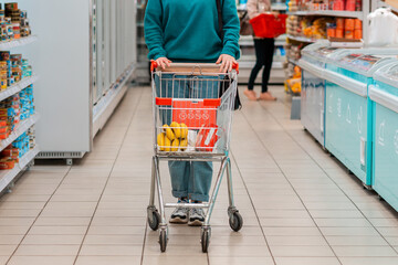 A woman in casual clothing, pushing a grocery cart around the store. Legs and cart close-up. The concept of purchasing goods and shopping