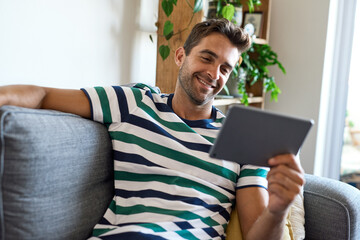 Smiling young man sitting at home using a digital tablet