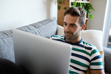 Young man relaxing on his sofa using a laptop