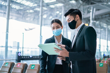 Wall Mural - New normal and social distancing concept.Businessman and businesswoman wearing face mask meeting during airline flight status and sitting with distance during coronavirus 2019 outbreak at airport