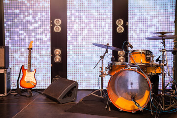 MUSICAL INSTRUMENTS DRUMS AND GUITAR ON STAGE, IN BACKGROUND LIGHT BARS. MUSICAL PERFORMANCE.