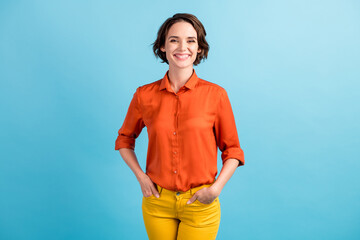 Photo of attractive amazing pretty business lady bob hairdo good mood smiling white teeth charming hands pockets yellow pants wear orange office shirt isolated blue color background