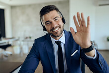 Happy Businessman Waving While Working In The Office And Looking At Camera.