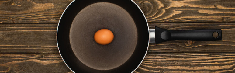 Wall Mural - top view of raw chicken egg in frying pan on wooden surface, panoramic shot