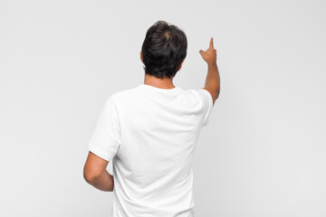 young latin handsome man standing and pointing to object on copy space, rear view