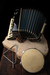 Old accordion, tambourine and triangle on rustic wooden surface with black background and Low key lighting, selective focus.