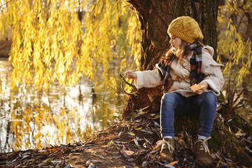 Cheerful preschooler little girl in coat and yellow hat with autumn leaves in the park. Child portrait. Cute kid girl 4-5 year old posing outdoors, has happy face. Walking in park. Childhood.