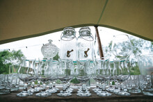 Front View Of Empty Glasses And Table Bar Catering. Preparing For Outdoor Celebration Under Canopy. Bottles And Goblets For Alcohol, Strong Drinks And Cocktails. Concept Of Getting Ready For Feast.
