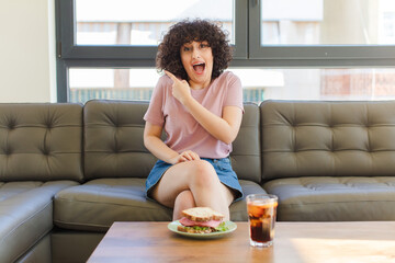 Wall Mural - young pretty arab woman having a sandwich sitting on a sofa at home