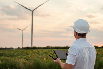 engineer is checking energy production on wind turbine. worker in windmills park in helmet and with 