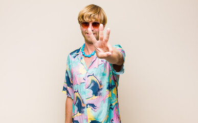 Wall Mural - blonde adult caucasic man smiling and looking friendly, showing number three or third with hand forward, counting down