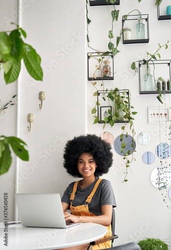 Happy hipster African American young woman with Afro hair using laptop computer in cafe, remote studying, working online, looking at camera sitting in cozy modern coffee shop table, vertical portrait Tableau sur Toile