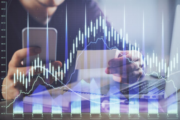 Double exposure of man's hands holding and using a phone and financial graph drawing. Analysis concept.