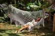 Vacation concept. Enjoying the summer. Young woman  resting in comfortable macrame hammock at green garden