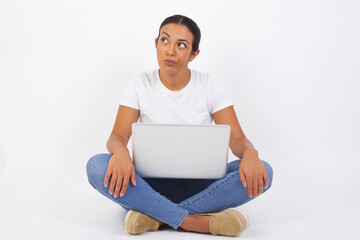 Wall Mural - Pleasant looking young female student, looks pensively aside, plans actions after university, imagines what to do. Clever woman thinks over about new project. Copy space on gray.