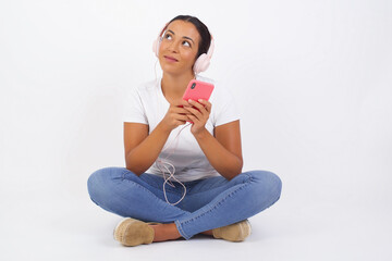 Wall Mural - Image of a happy young beautiful woman posing isolated over bright background listening to music with earphones using mobile phone.