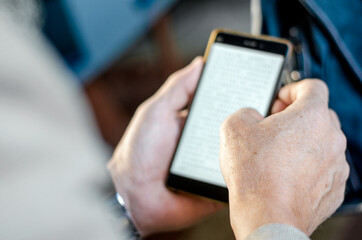 Closeup view of male hands touching mobile phone. Man using a smartphone holding finger on the screen. Man reads an ebook on his phone in public transport.