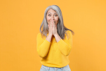 Wall Mural - Shocked amazed surprised excited cheerful gray-haired asian woman wearing casual clothes standing covering mouth with hands looking camera isolated on bright yellow colour background, studio portrait.