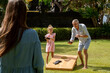 Happy family playing cornhole game outdoor on sunny summer day. Parents and children playing bean bag toss
