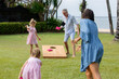 Happy family playing cornhole game by the sea on sunny summer day. Parents and children playing bean bag toss