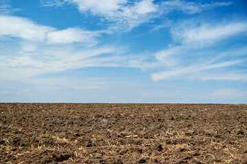 plowed field and blue sky, soil and clouds of a bright sunny day - concept of agriculture