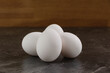 Vier weiße Eier für die Zubereitung in der Küche auf einer dunklen Arbeitsplatte vor einem Holz-Hintergrund