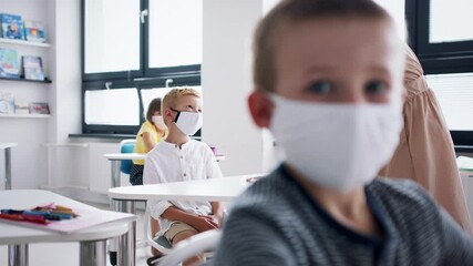 Wall Mural - Teacher and children with face masks indoors in classroom, disinfecting desks.