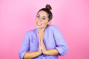 Young beautiful woman wearing glasses over isolated pink background begging and praying with hands together with hope expression on face very emotional and worried