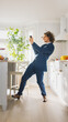 © Gorodenkoff - Happy Young Man with Long Hair Dancing at Home while Wearing Blue Business Suit. He is Listening to Music on a Mobile. Energetic Man Using Smartphone in a Kitchen with Healthy Vegetables.