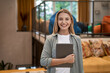 © Kostiantyn - Portrait of a young cheerful caucasian woman, female office worker holding digital tablet and looking at camera while standing in the modern office