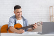 © Prostock-studio - Smiling young man watching online lesson, playing guitar and makes notes