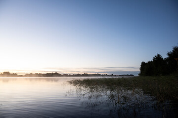 Wall Mural - morning haze rises over the lake at sunrise