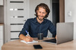 © uladzislaulineu - Handsome man with smile makes notes in notebook and works at laptop