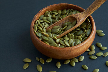 pumpkin seeds in a wooden bowl and vintage scoop. Close up on a black background. copy space for text