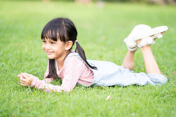 a 5 years old asian little girl is smiling and laying down on the grass in the park with happy momen