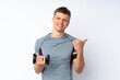 © luismolinero - Young sport man with weightlifting over isolated white wall pointing to the side to present a product