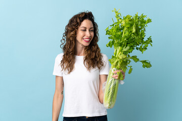 Wall Mural - Young woman holding a celery isolated on blue background with happy expression