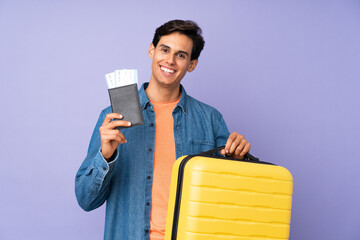 Man over isolated purple background in vacation with suitcase and passport