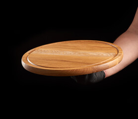 male hand in black latex glove holds round empty wooden pizza board