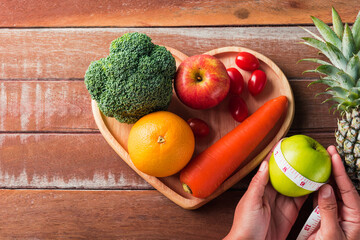 World food day, Top view of various fresh organic fruit and vegetable in heart plate and woman use hands hold the plate, studio shot on wooden table, Healthy vegetarian food concept