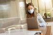 © goodluz - Young woman with face mask working in office