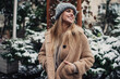 © BullRun - Cheerful Caucasian hipster girl 20 years old smiling at snowy street enjoying leisure time for winter walking, happy female tourist in eco coat and knitted hat enjoying cold season for travelling