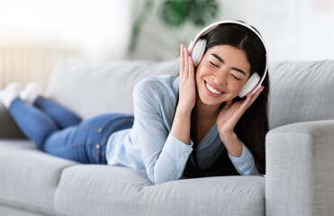 Wall Mural - Time To Relax. Cheerful Asian Girl In Headphones Listening Music On Couch