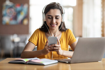 Wall Mural - Young girl student sitting at cafe, using laptop and smartphone