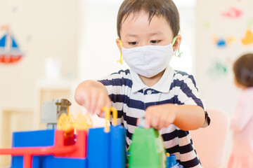 Asian toddler boy playing toy in kids club at hotel.3.5 years old boy child wearing face mask in Day care.Covid-19 coronavirus.Stay home.Social distancing in school.Back to school.New normal behavior.