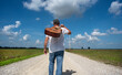 © Jon - Man walking on one lane country dirt road carrying acoustic guitar over shoulder, blue sky, clouds, travel, traveling, independent, freedom, music, musician, musical instrument