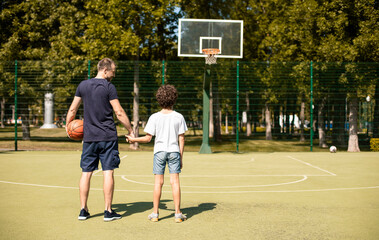 Wall Mural - Man posing with son on basketball pitch back view